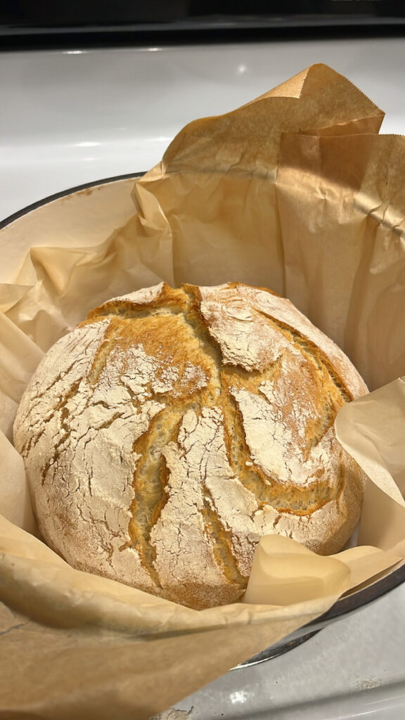 Homemade bread sits in a white dutch oven on a stovetop