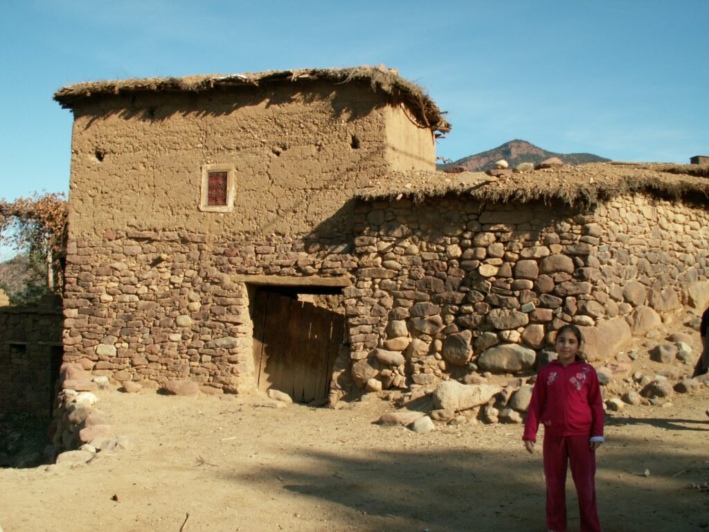Girl in matching pink outfit set stands in front of a stone and straw home in the Atlas Mountains of Morocco