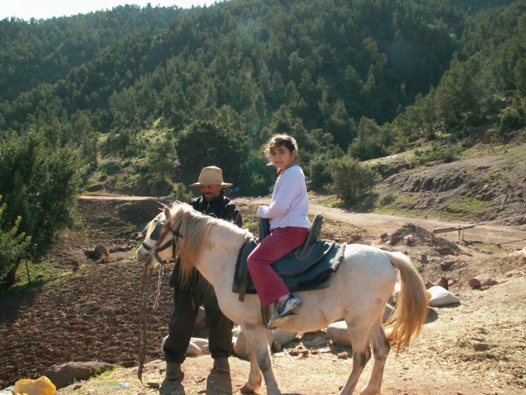 Girl rides on a small pony led by a guide through the Atlas Mountains in Morocco