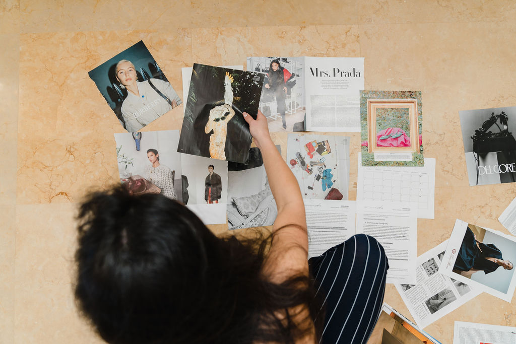 Woman sits on the floor and sorts through loose torn out pages of a Vogue magazine