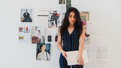 Brunette woman in pinstriped navy blue matching set stands in front of vogue magazine pages taped to a wall
