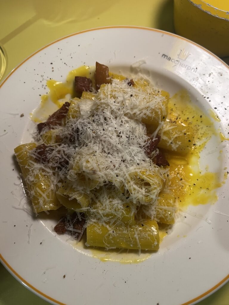 Plate of carbonara pasta is topped with shredded parmesan cheese