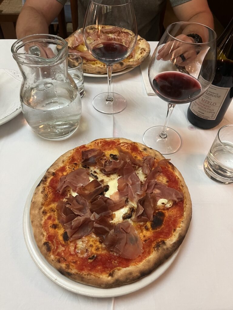 Two plates of pizza sit on a table with two glasses and a bottle of wine
