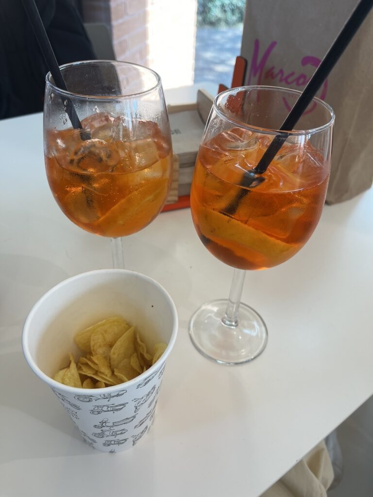 Two glasses of Aperol Spritz cocktails sit next to a cup of potato chips