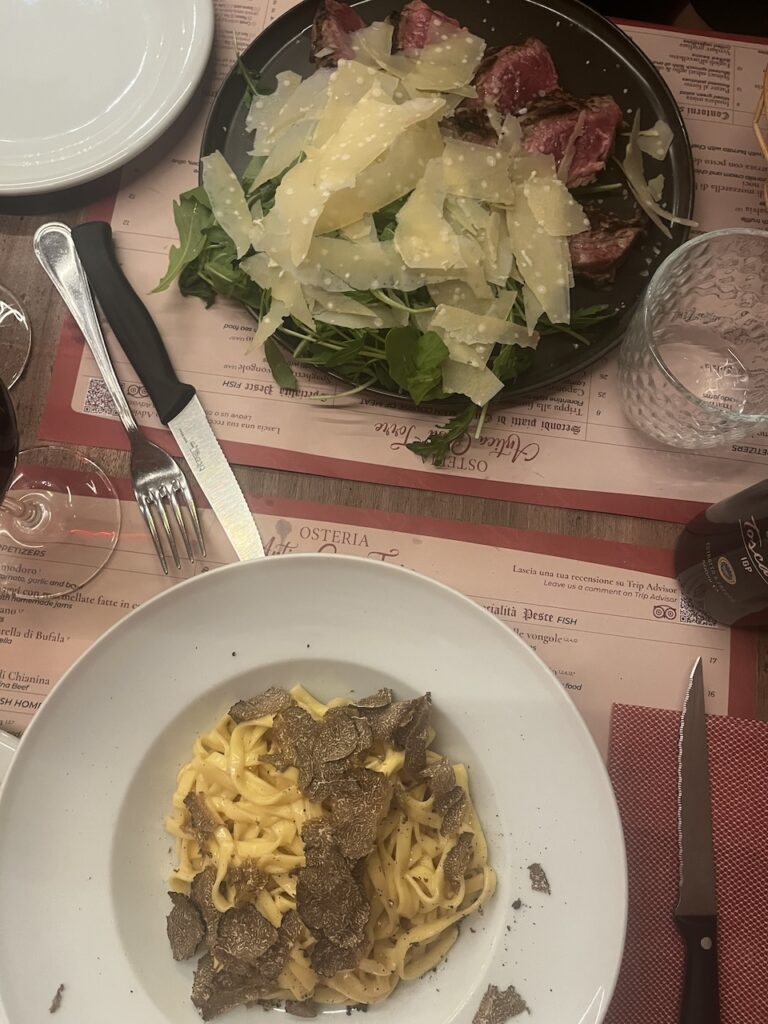 Plate of parmesan salad and steak sits across from a plate of truffle pasta at I'Brindellone in Florence, Italy