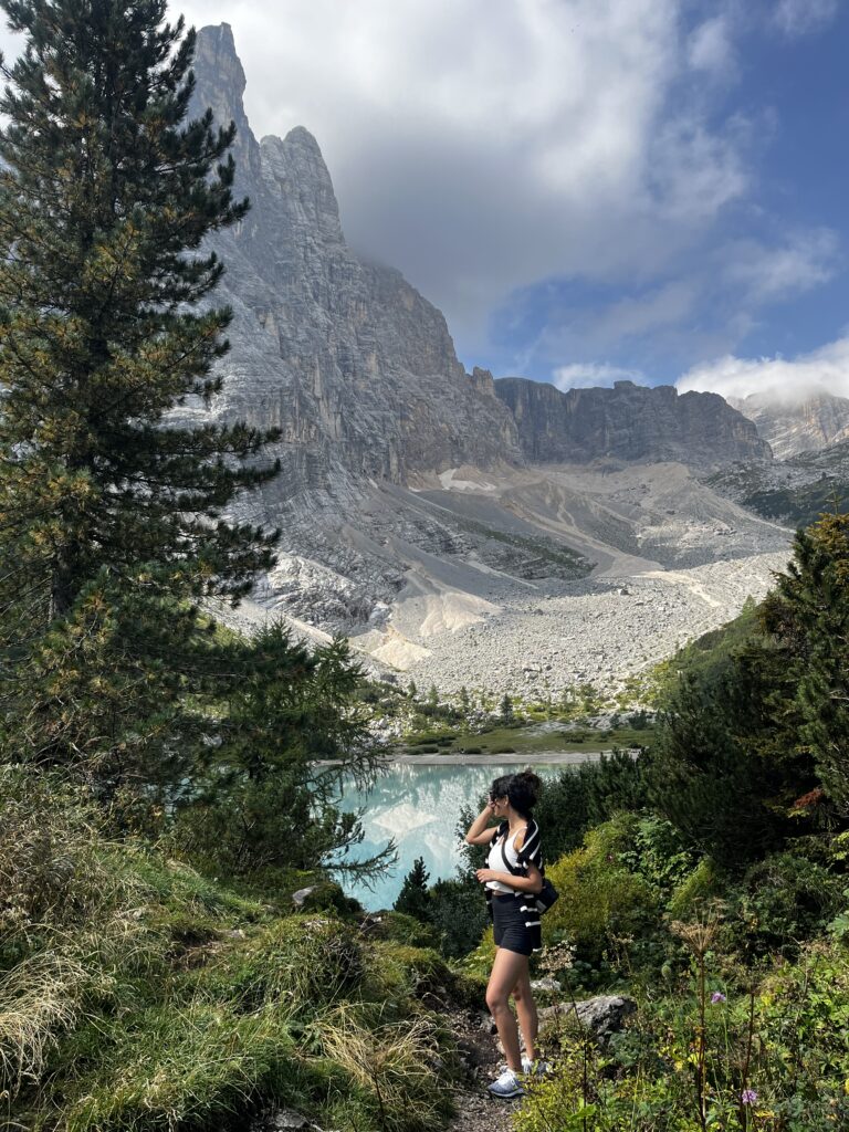 Woman stands in front of Lago di Sorapis with mountains in the background in the Dolomites region of northern Italy