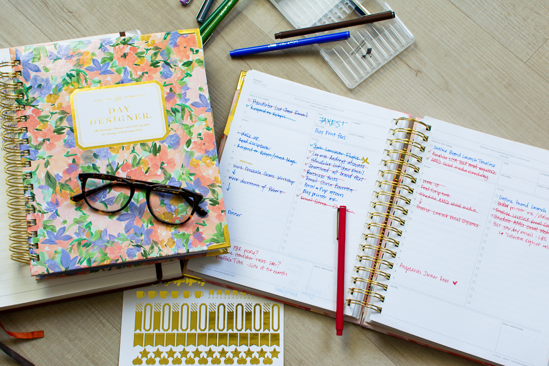 Day Designer planner sits open next to a second floral print Day Designer planner next to stickers, pens, and reading glasses